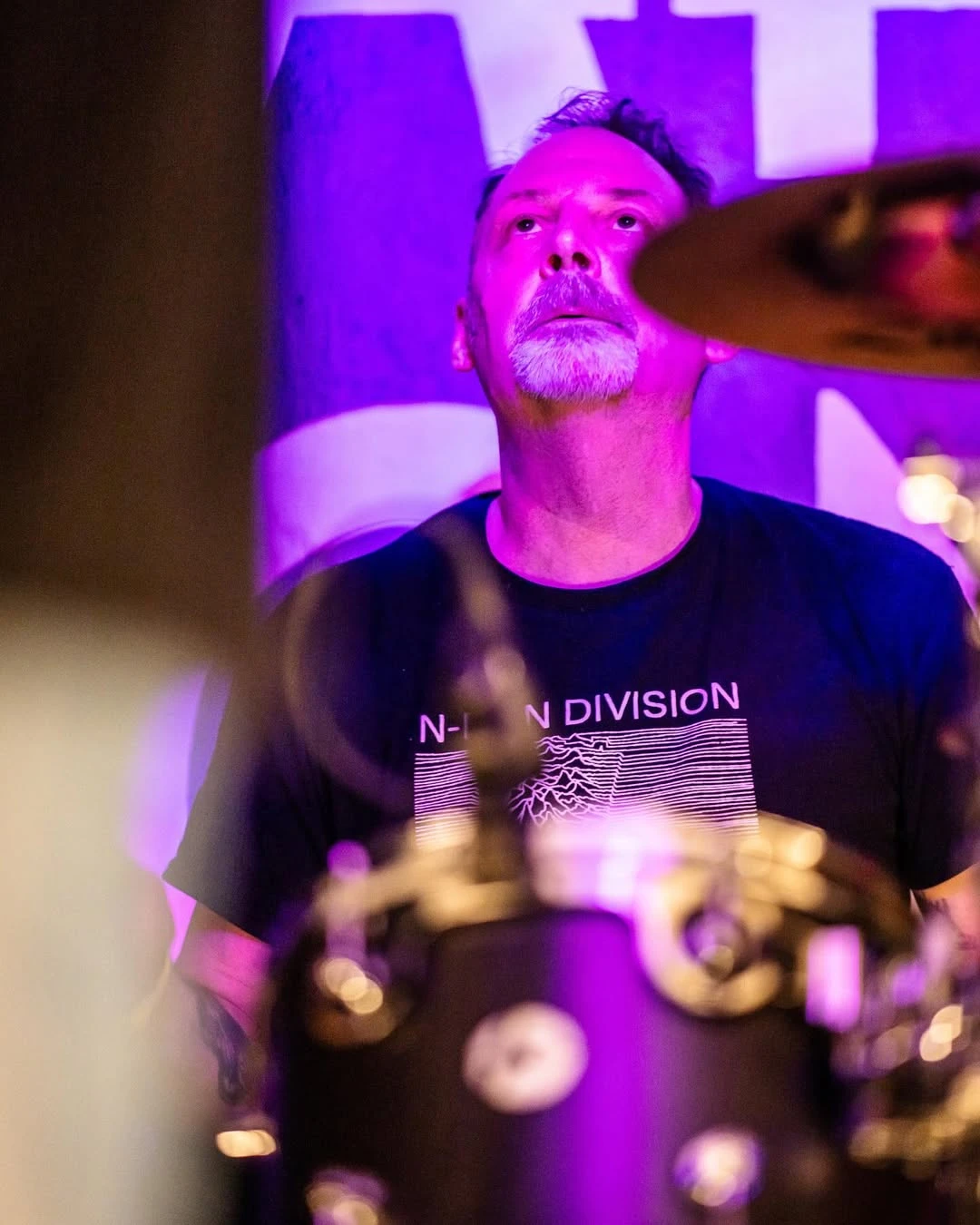 Drummer behind the kit, bathed in purple light