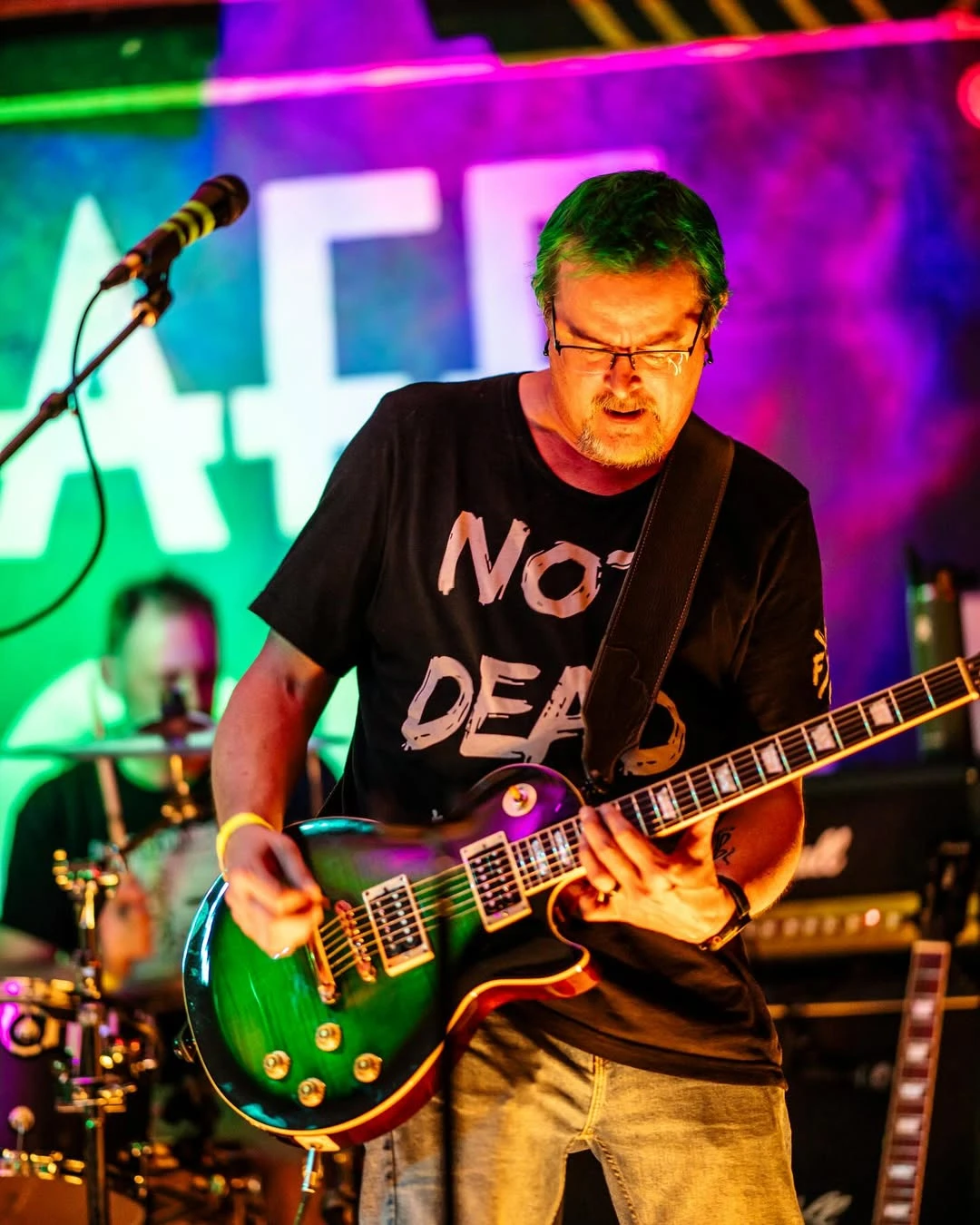 Guitarist in a Not Dead shirt playing a green Les Paul