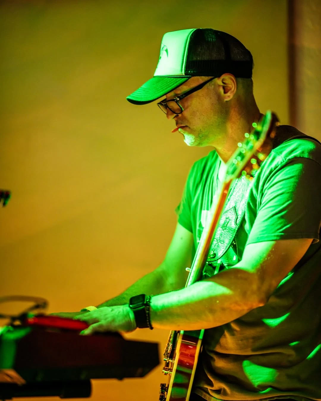Playing keys with a guitar slung on, in green light