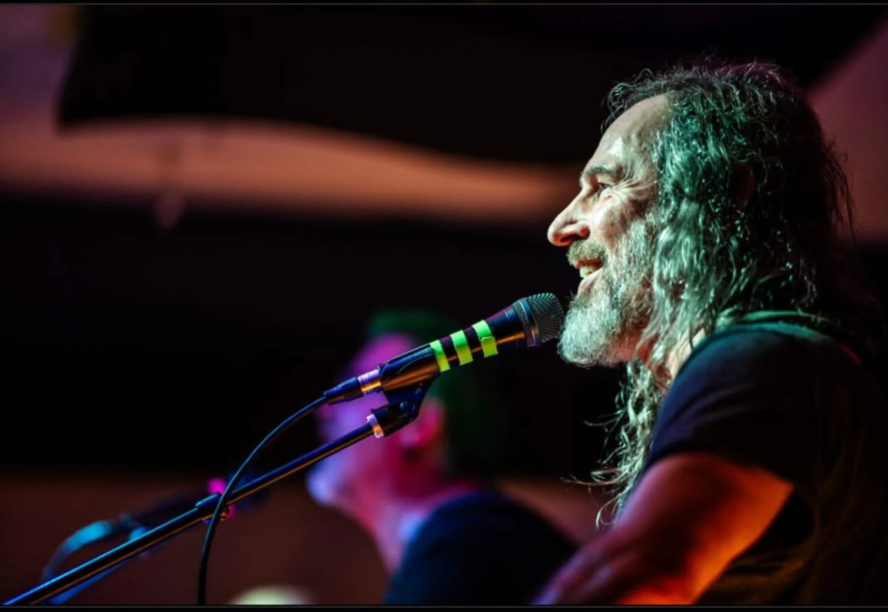 Singing at the mic, smiling, under red and purple light